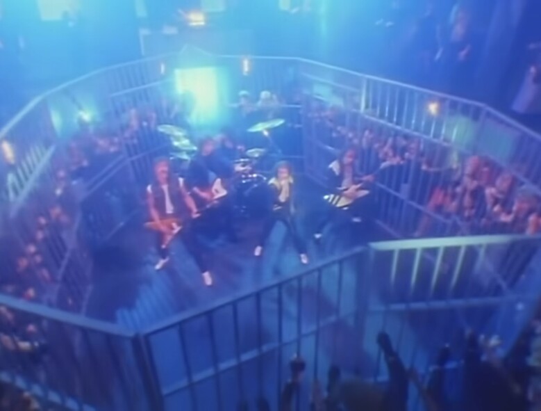 Кадр из клипа «Rock You Like a Hurricane» (1984). Группа играет в клетке посреди толпы — один из самых знаковых образов в истории рока.
